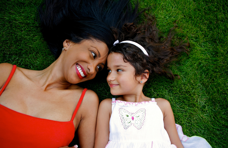 Mom and daughter lying on the grass looking at each other