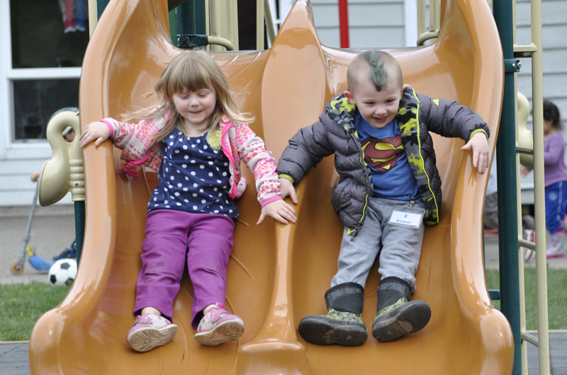 A boy and a girl go down the slide together