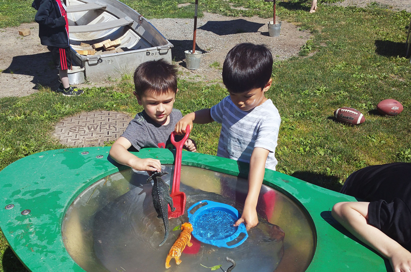 Two little boys playing in a water tub outside