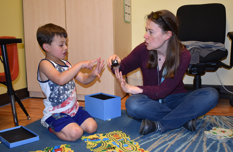 A young boy and a therapist play with toys on the ground