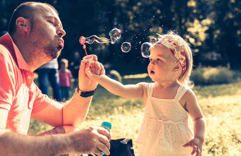 Dad and little girl playing with bubbles outside