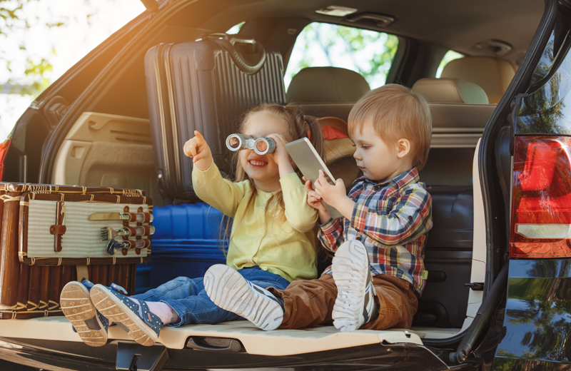 Two small children look out from the back of a car