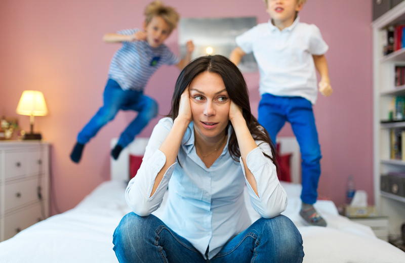 Stressed mom looks on while her sons jump on the bed