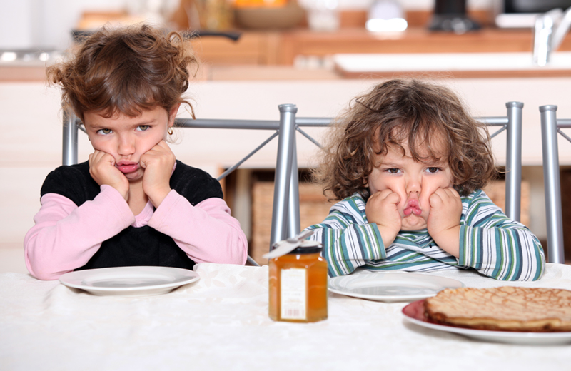 Two young children pouting at the table