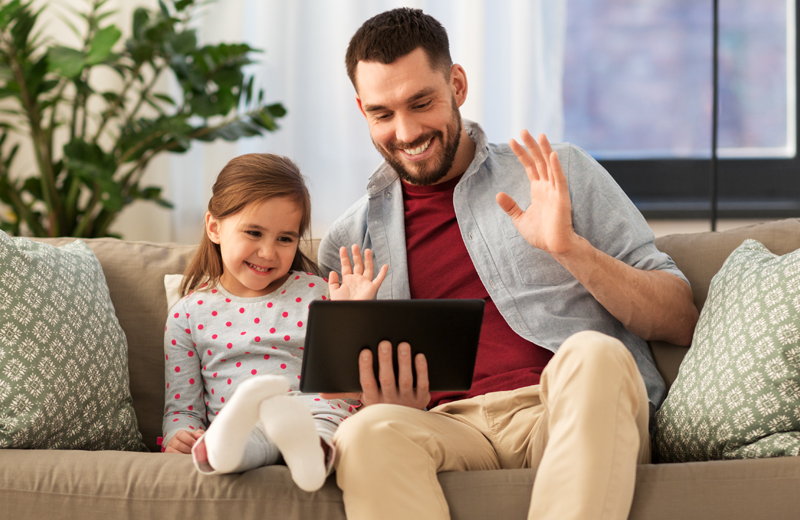 Man and littler girl video chatting on the couch