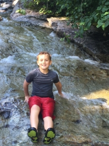 boy sitting on water and rocks